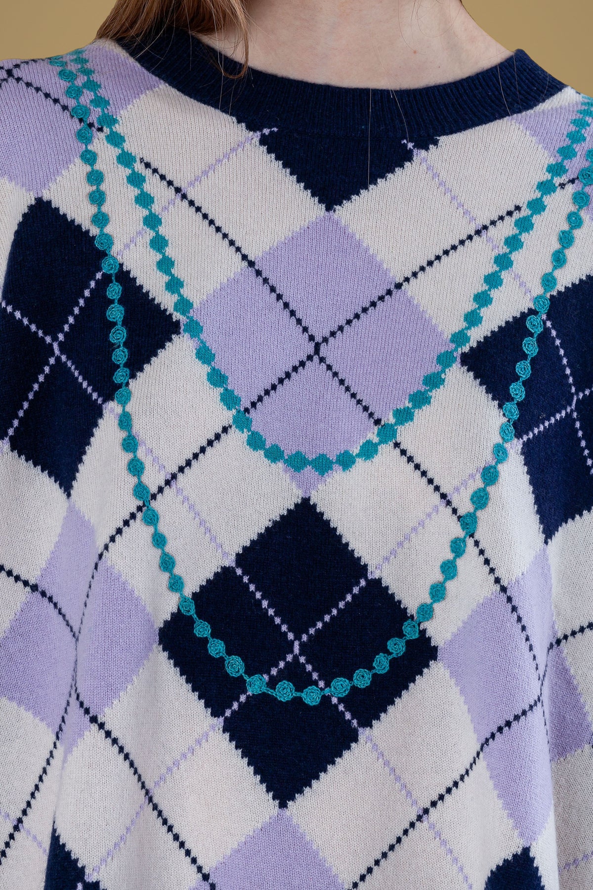 Close-up of embroidered pearl necklace on argyle knit