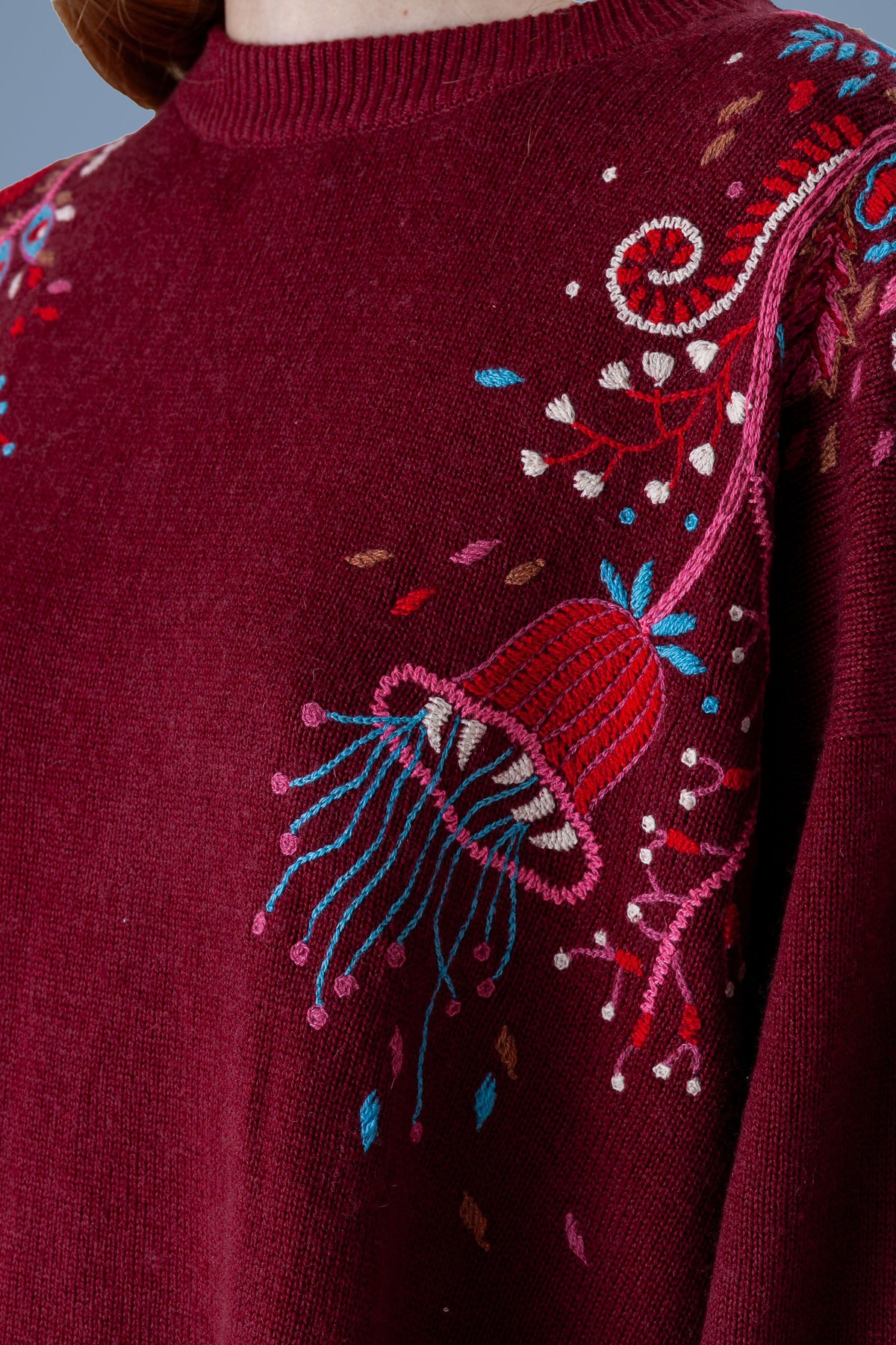 Close-up of hand embroidery on burgundy knit: bell flower and stems