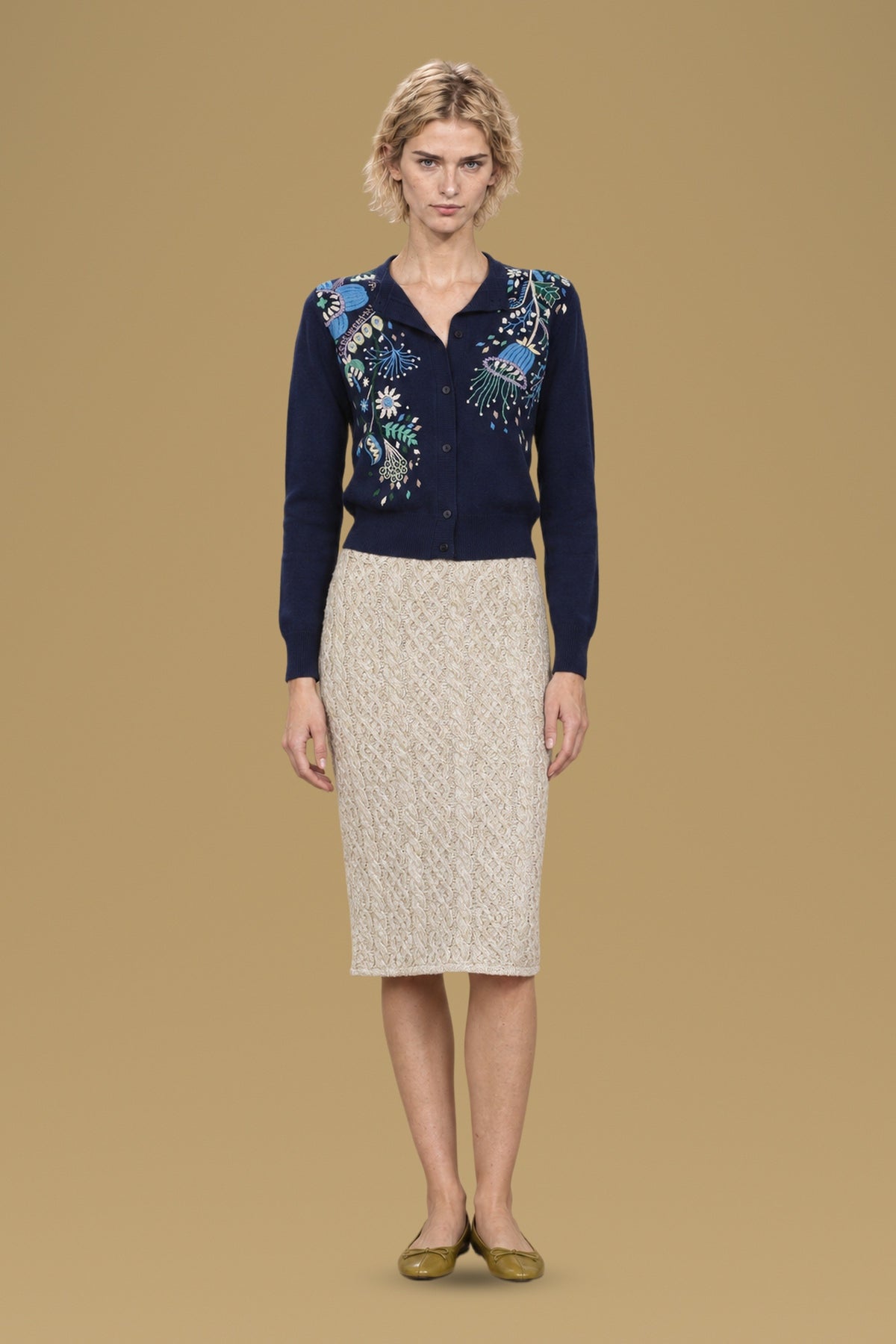 Navy hand-embroidered Rebecchina cardigan, front view, worn with a cream cable-knit skirt