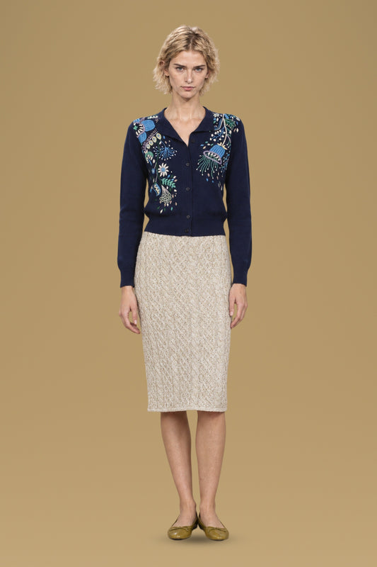 Navy hand-embroidered Rebecchina cardigan, front view, worn with a cream cable-knit skirt